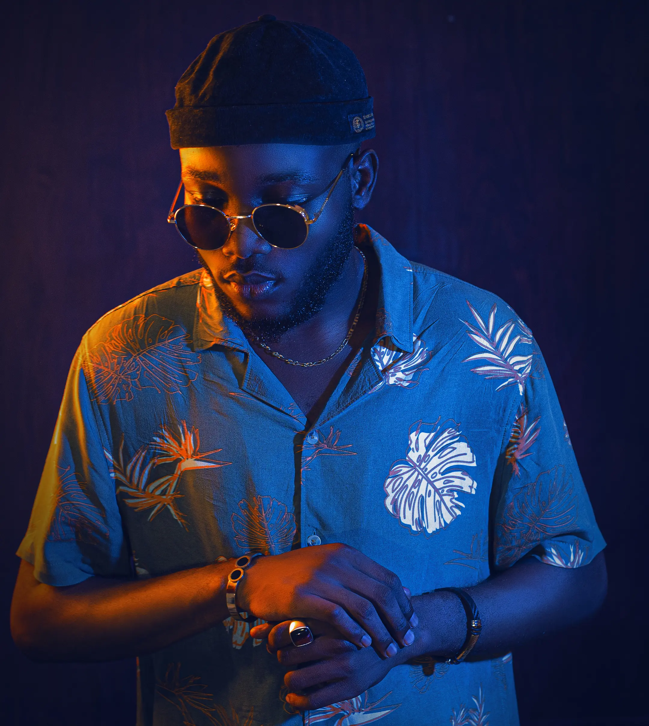 Portrait de Kékéli, casquette beige et lunettes noires, fond bleu nuit
